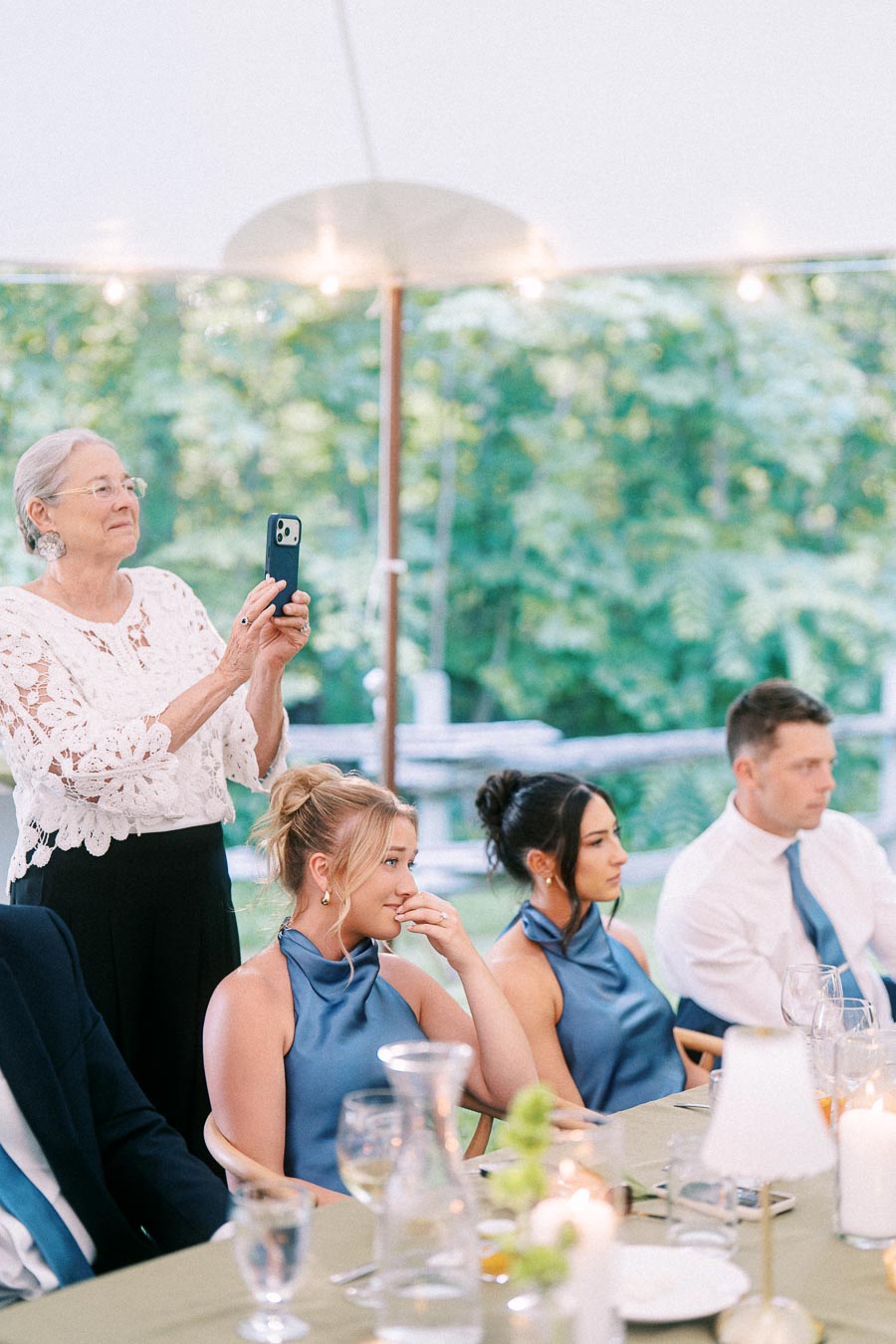 Wedding guests seated at a tented outdoor reception near Chatham-Kent, Ontario, while an older woman records with a smartphone.