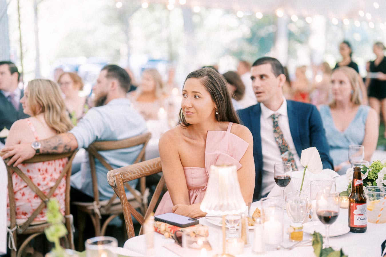 Wedding guests seated at a tented outdoor reception dinner on a private estate near Chatham-Kent, Ontario, with candles, flowers, wine glasses, and warm string lights.