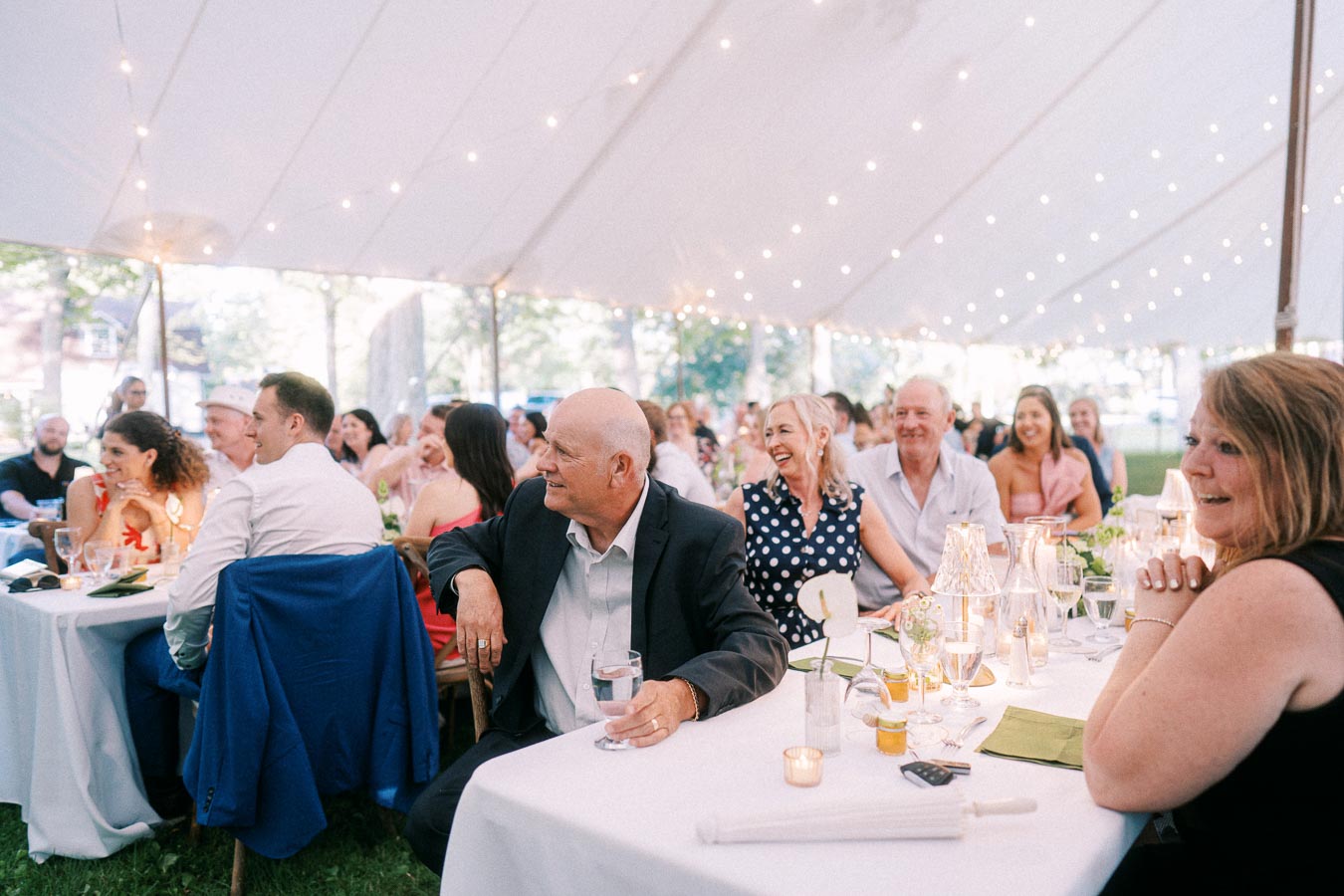 Wedding guests seated at a tented outdoor reception on a private farm estate near Chatham-Kent, Ontario, with string lights and table settings.