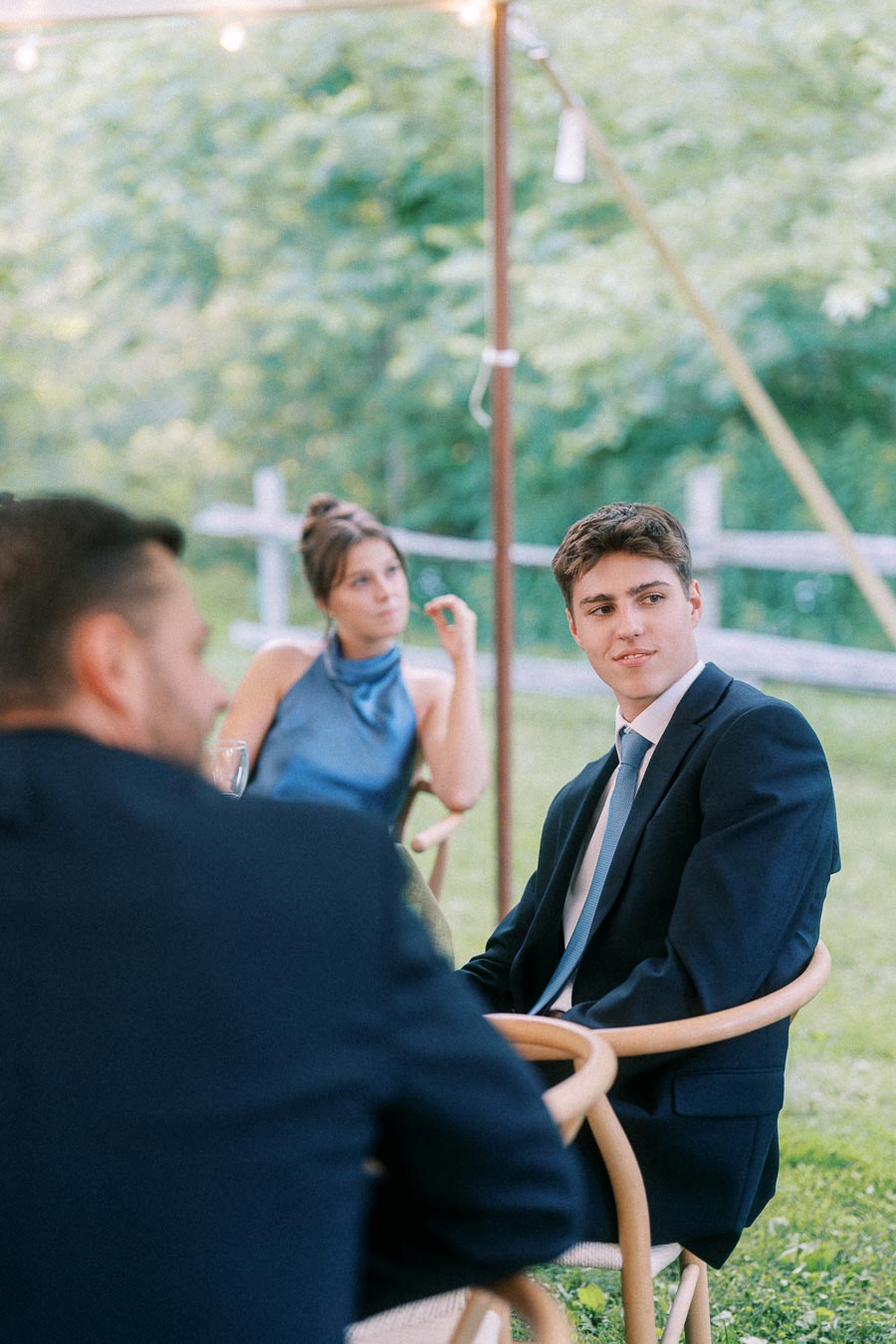 Guests seated at an outdoor tented farm wedding reception on private property near Chatham-Kent, Ontario, with trees and a fence behind them.