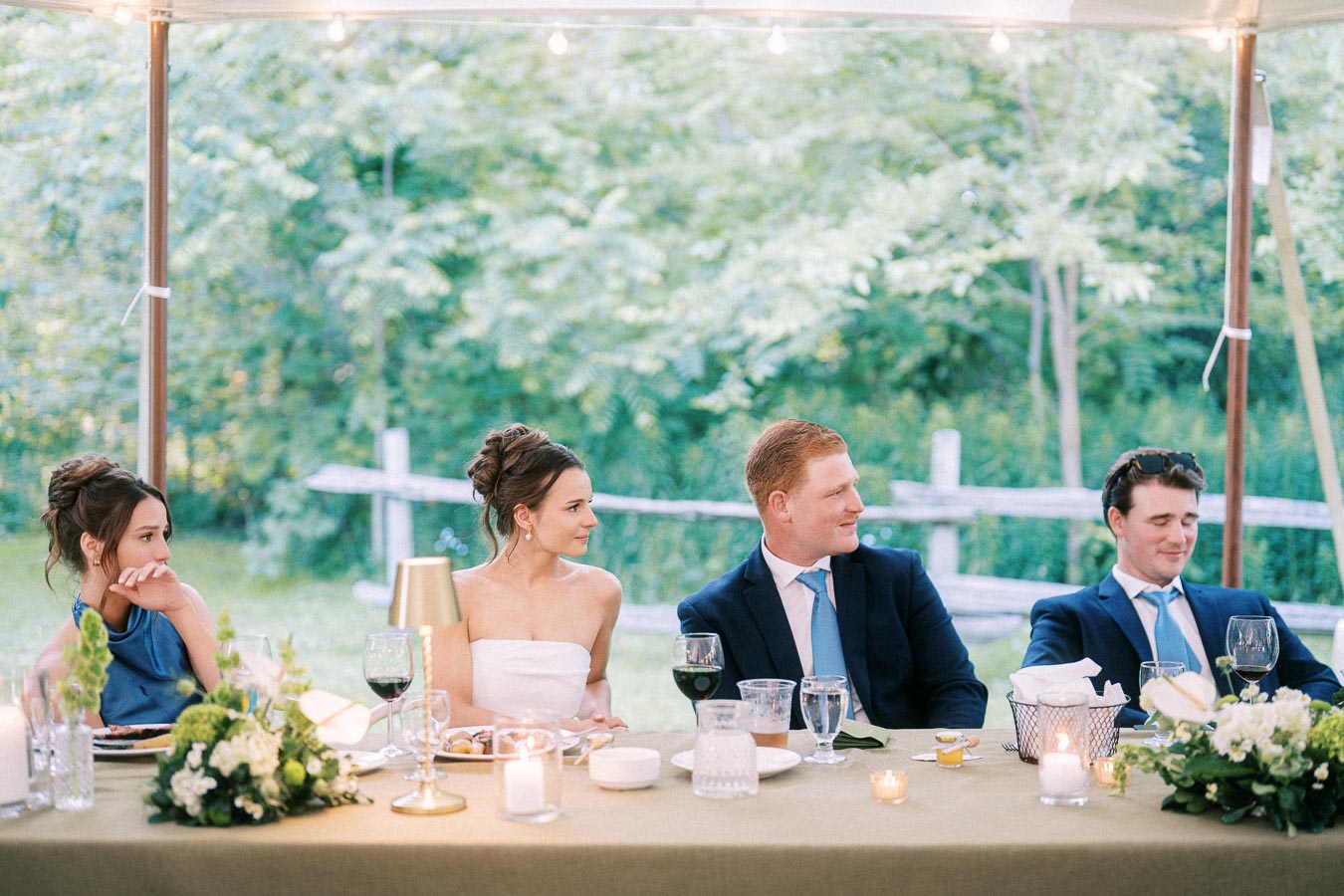 Bride, groom, and guests seated at a decorated dinner table under a wedding tent on a green farm property near Chatham-Kent, Ontario.