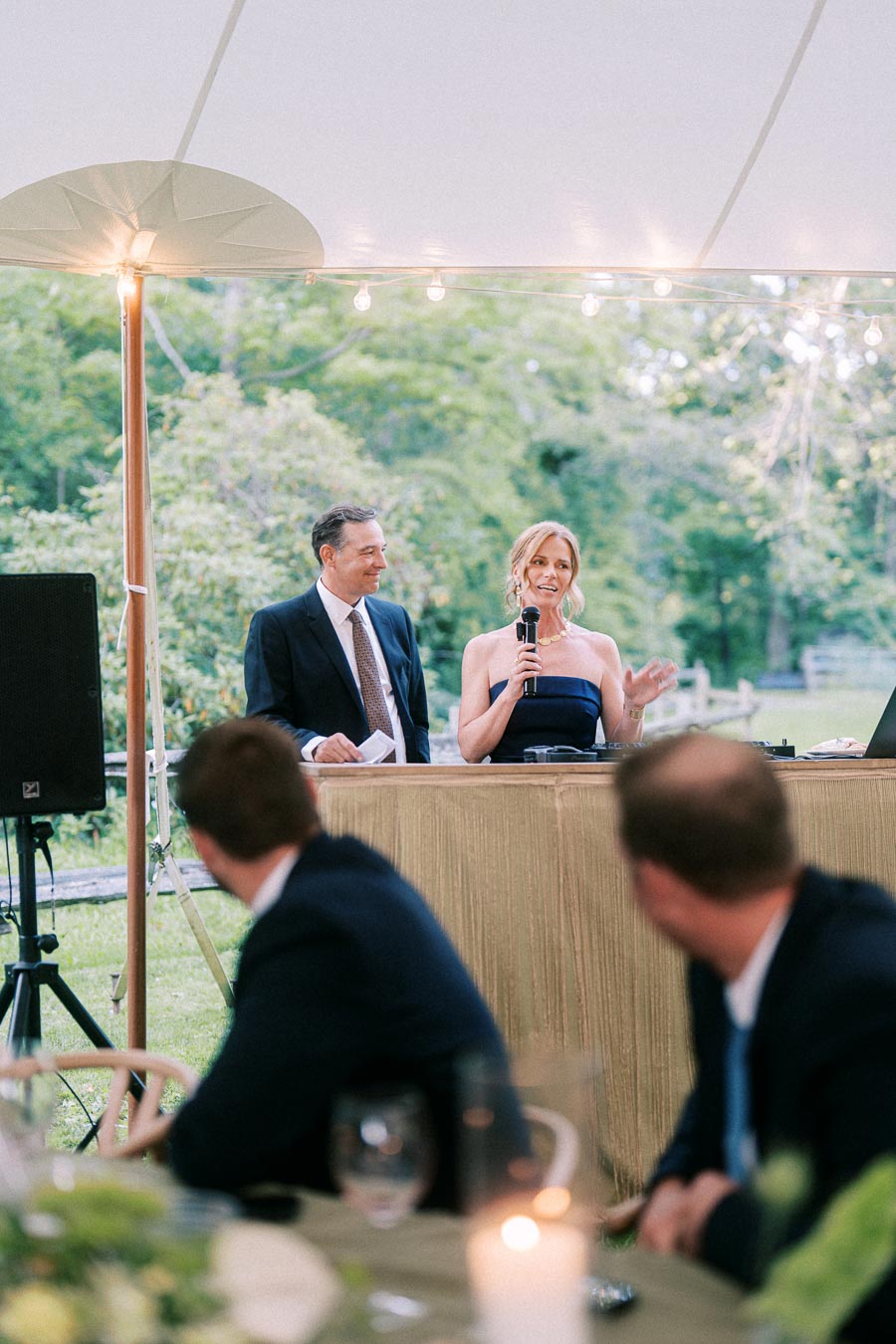 Woman giving a speech with a microphone beside a man under a wedding tent at a private estate farm near Chatham-Kent, Ontario.
