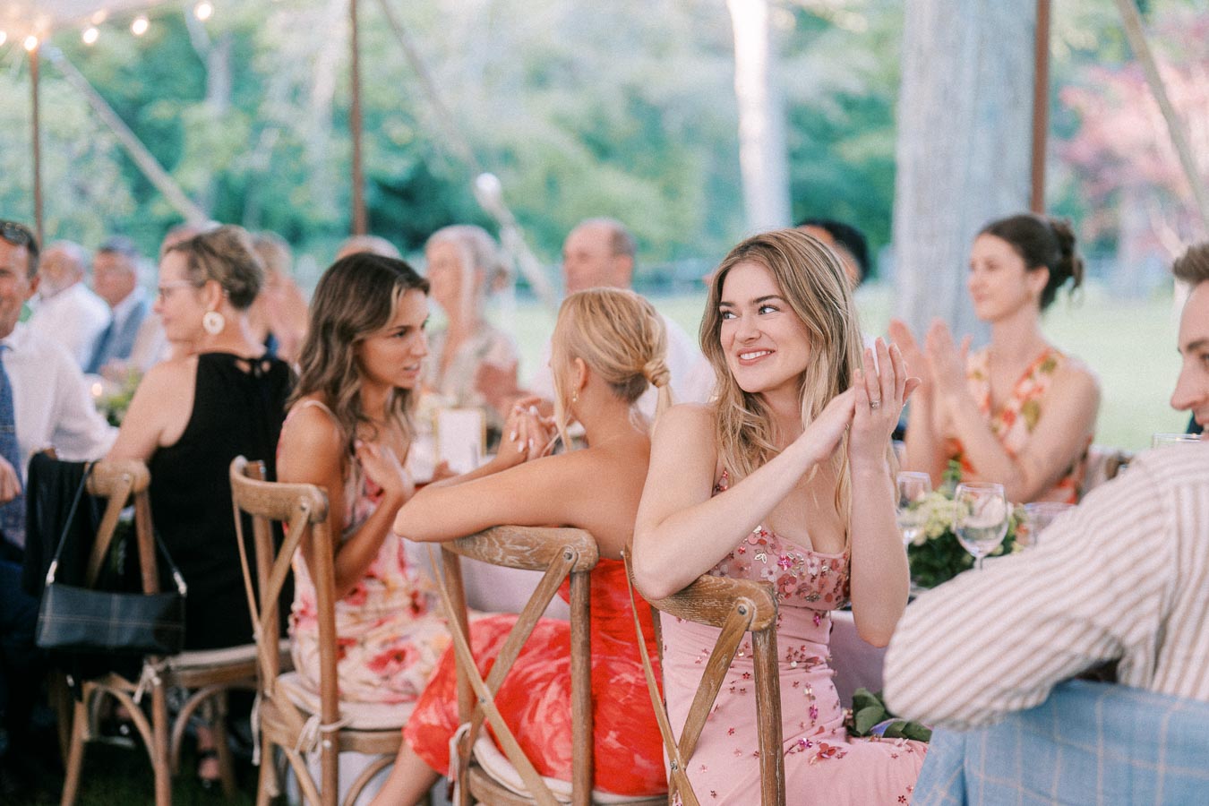 Guests seated at a tented outdoor wedding reception on a farm near Chatham-Kent, Ontario, with wooden chairs, flowers and glassware.