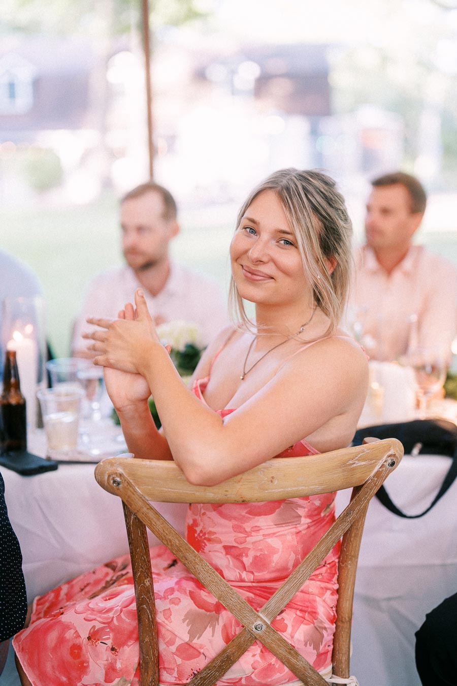 Smiling young woman in a pink floral dress seated at a wedding reception table under a tent near Chatham-Kent, Ontario.