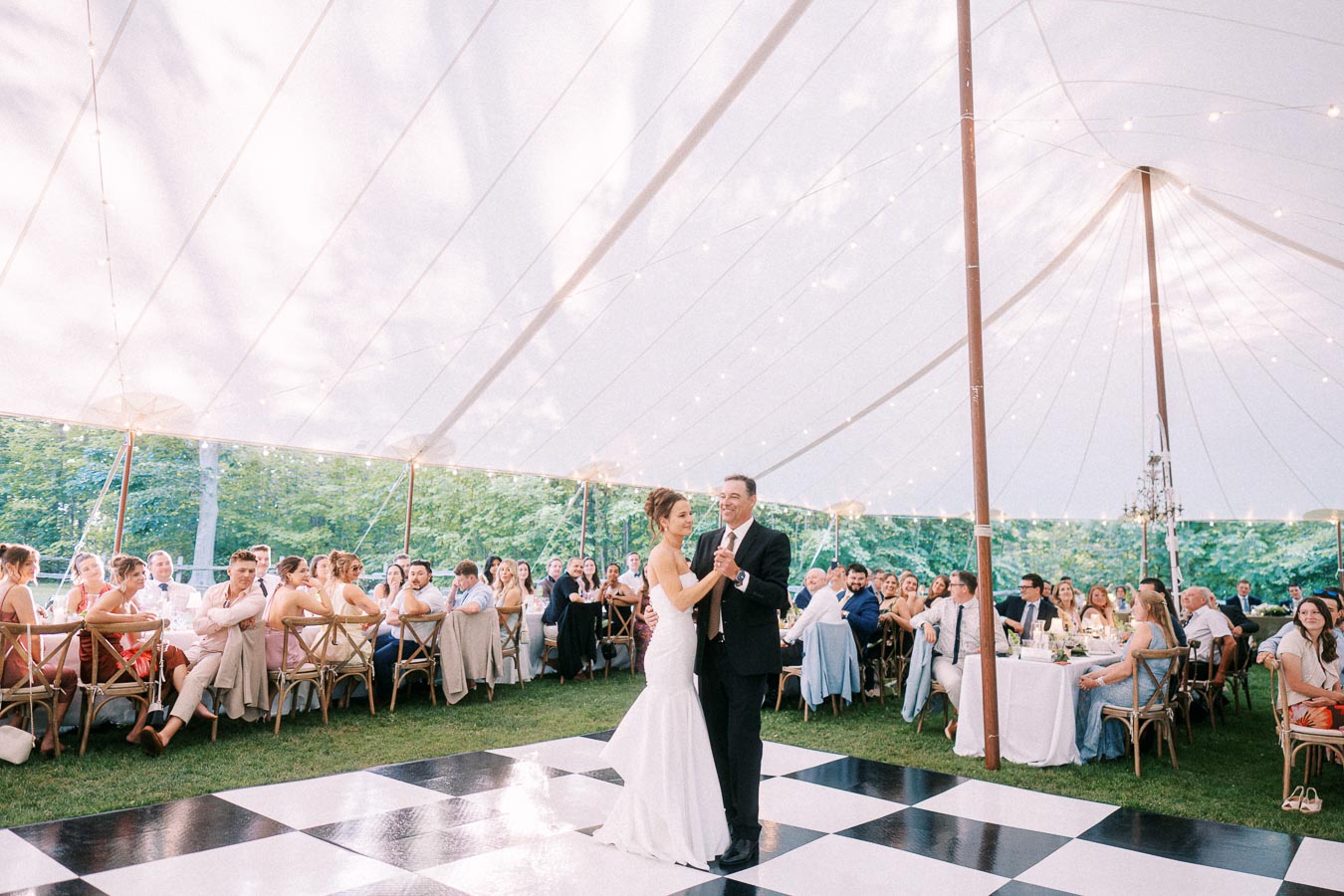 Bride and groom dancing on a checkered floor under a white reception tent with seated wedding guests near Chatham-Kent, Ontario.