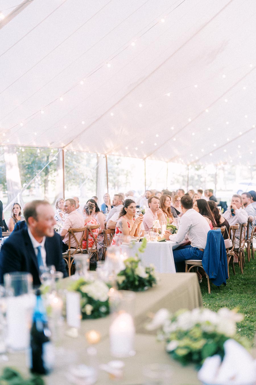 Wedding guests dining inside a white tent with string lights during an outdoor farm reception near Chatham-Kent, Ontario, Canada.