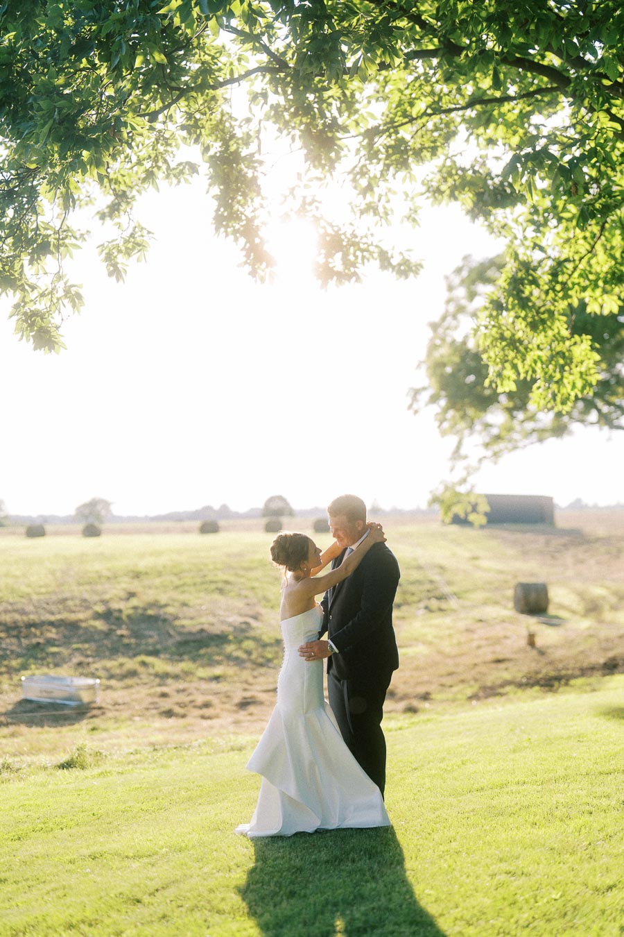 Bride and groom embracing on a sunlit farm field near Chatham-Kent, Ontario during an outdoor private estate wedding.