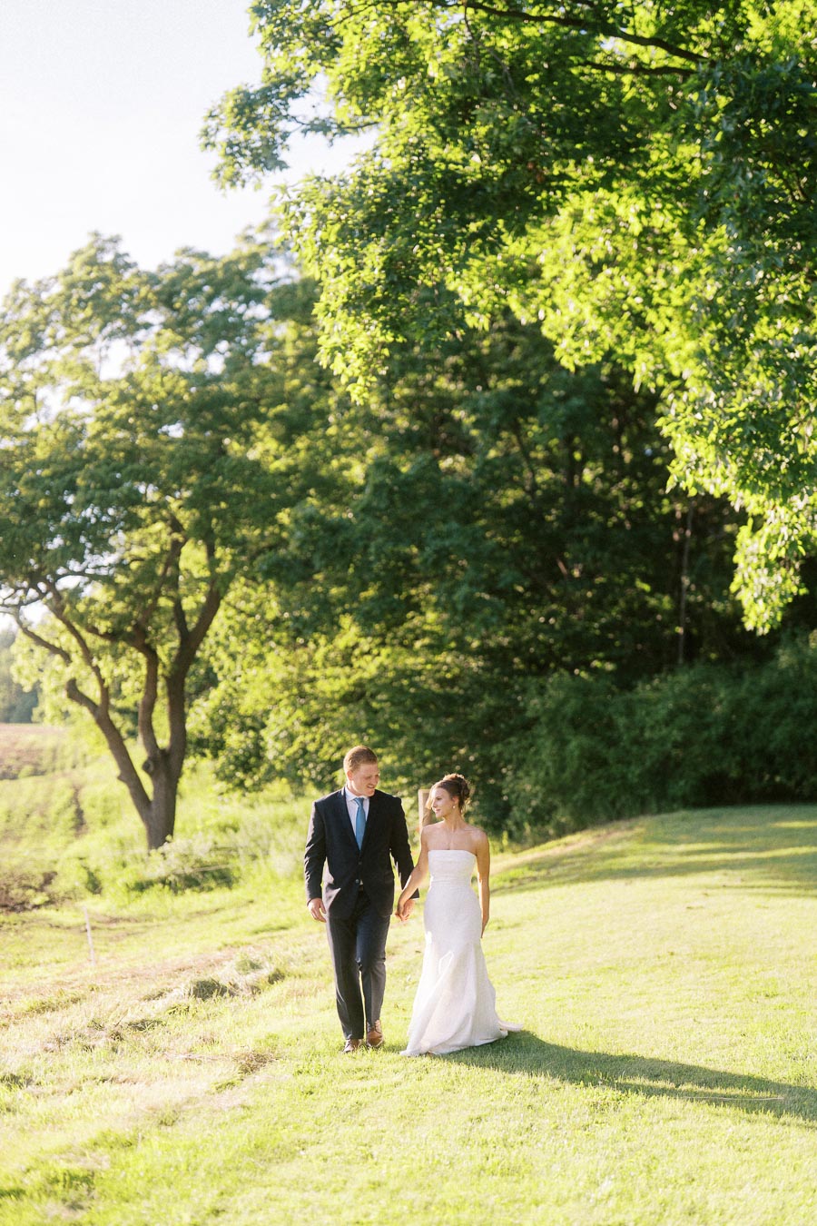 Bride and groom holding hands while walking on a grassy private estate farm near Chatham-Kent, Ontario, Canada.