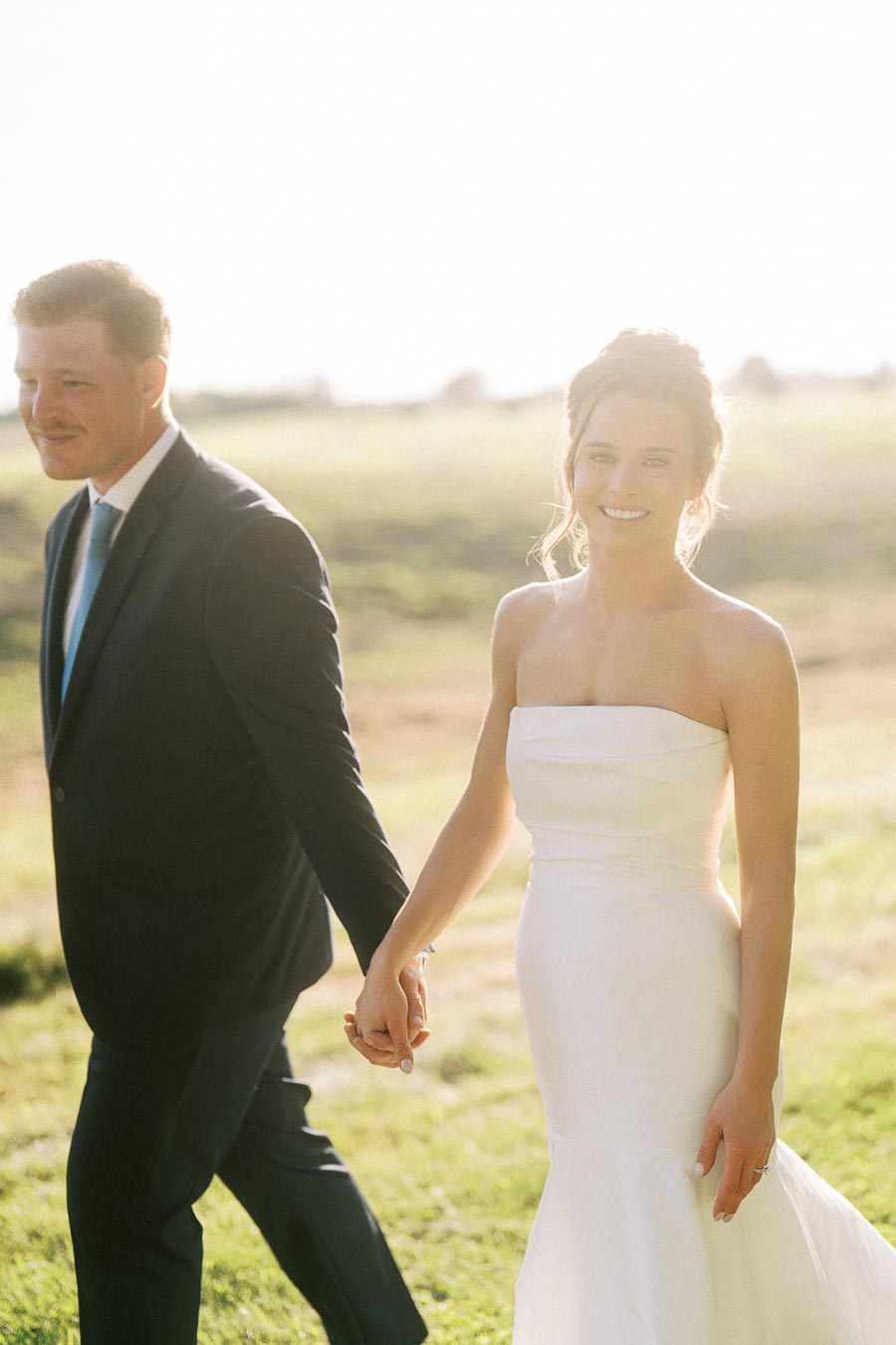 Bride and groom holding hands outdoors on a sunny farm field near Chatham-Kent, Ontario, Canada.