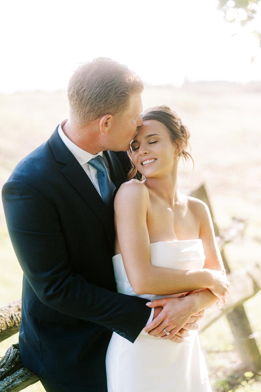 Groom kisses bride on the forehead during an outdoor farm wedding portrait near Chatham-Kent, Ontario, Canada.