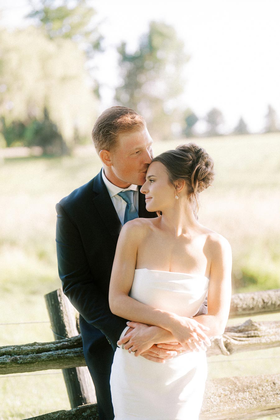 Bride and groom embrace by a rustic wooden fence during an outdoor farm wedding near Chatham-Kent, Ontario, Canada.