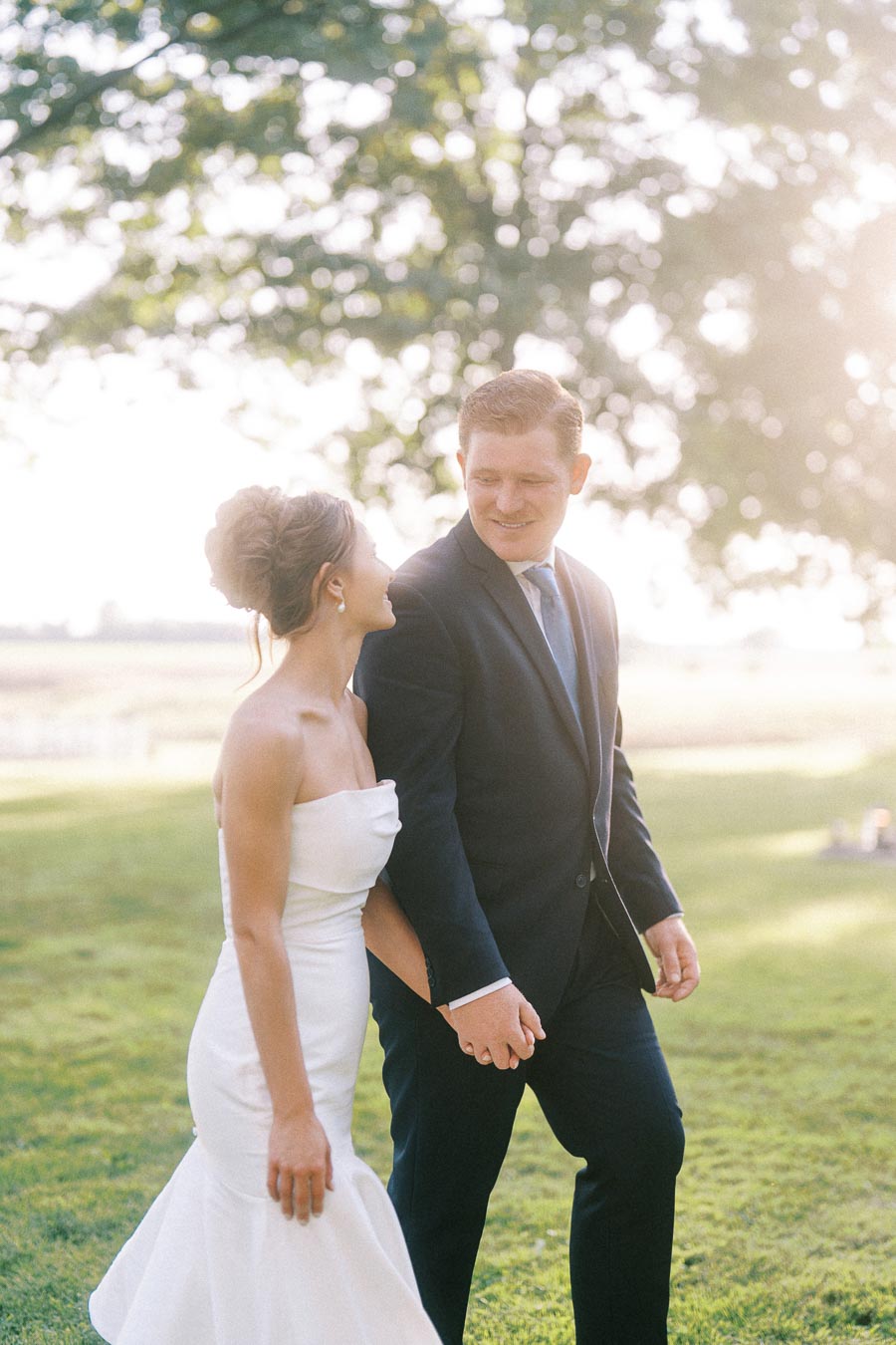 Bride and groom holding hands outdoors on a sunny farm lawn near Chatham-Kent, Ontario.