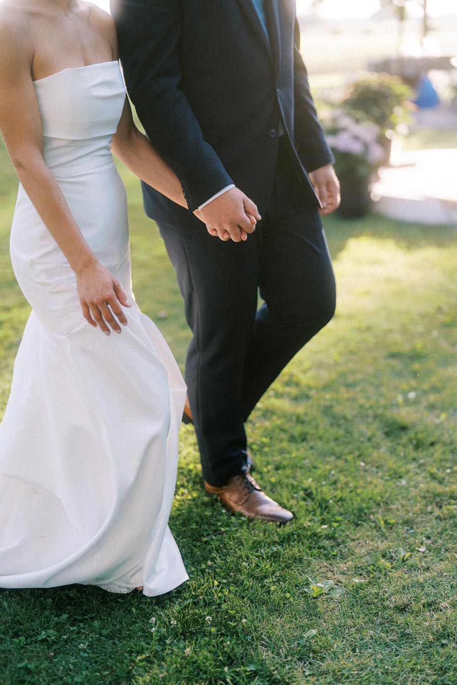 Bride and groom holding hands while walking on grass at an outdoor private estate wedding near Chatham-Kent, Ontario, Canada.