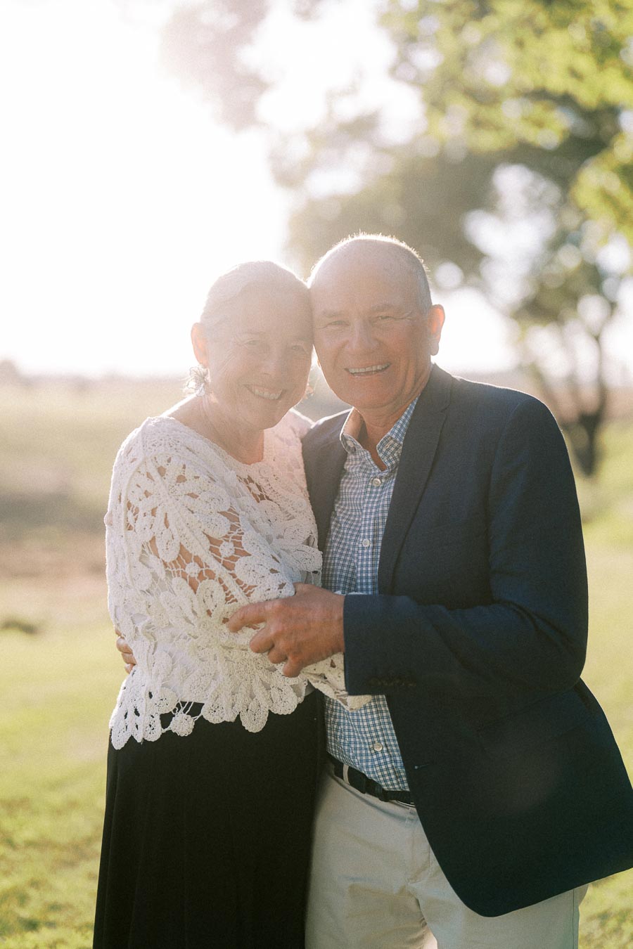 Smiling older couple embracing outdoors at a private estate farm wedding near Chatham-Kent, Ontario, Canada, with warm backlight and trees.