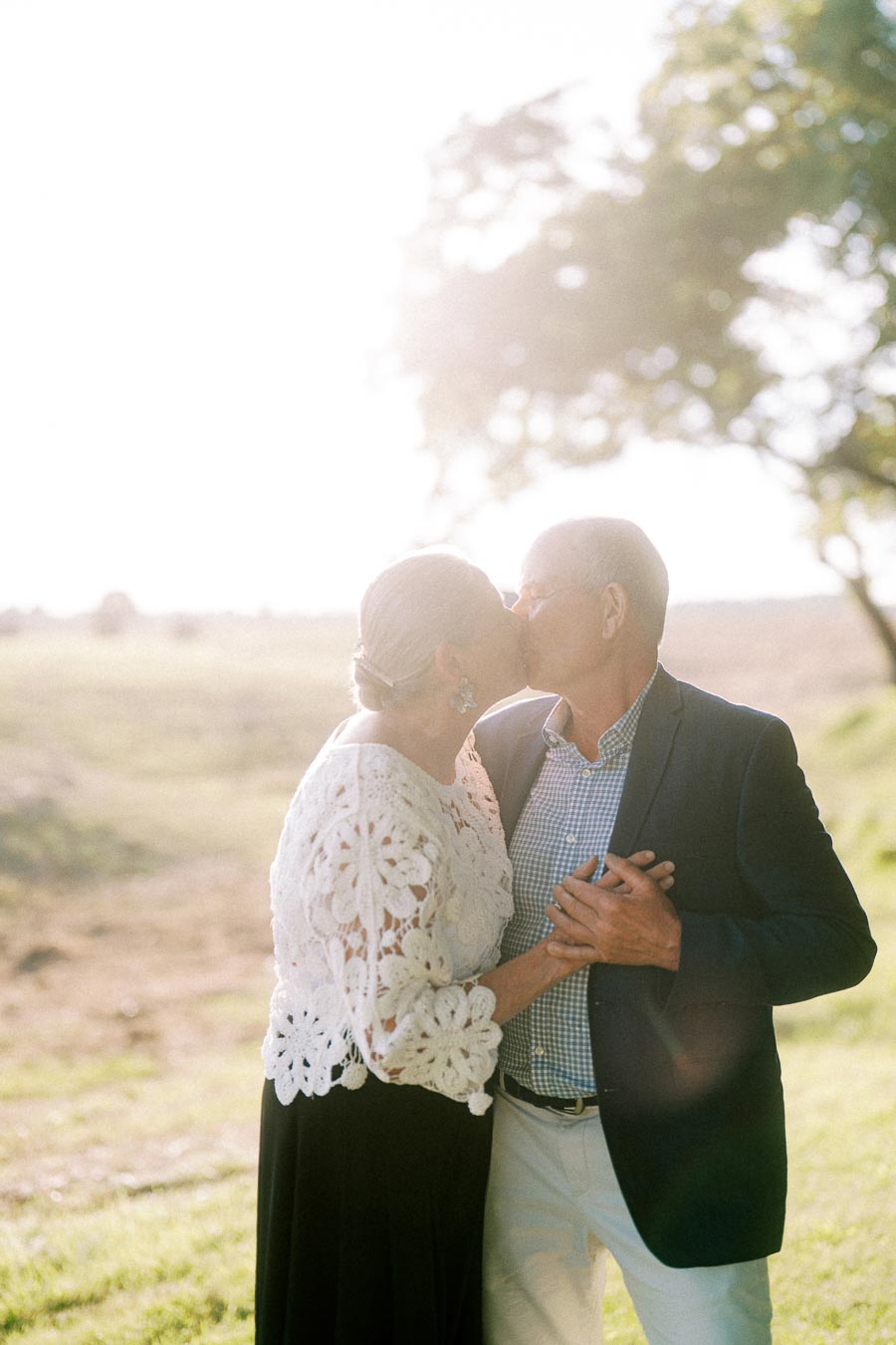 Older couple kissing and holding hands outdoors on a private farm estate near Chatham-Kent, Ontario, Canada, in warm sunset light.