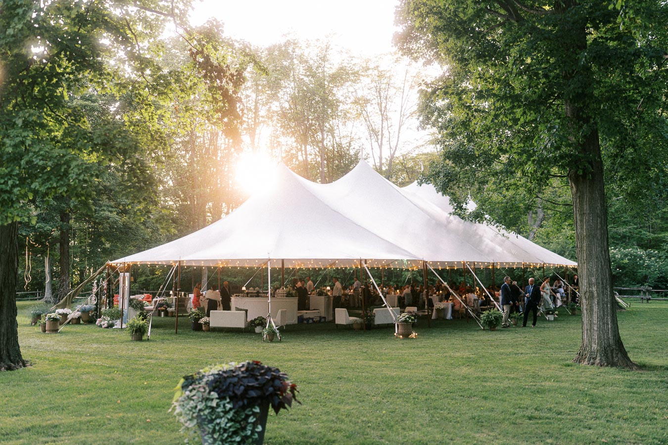 Outdoor tented wedding reception on a private estate lawn near Chatham-Kent, Ontario, with guests dining under a white canopy at sunset.