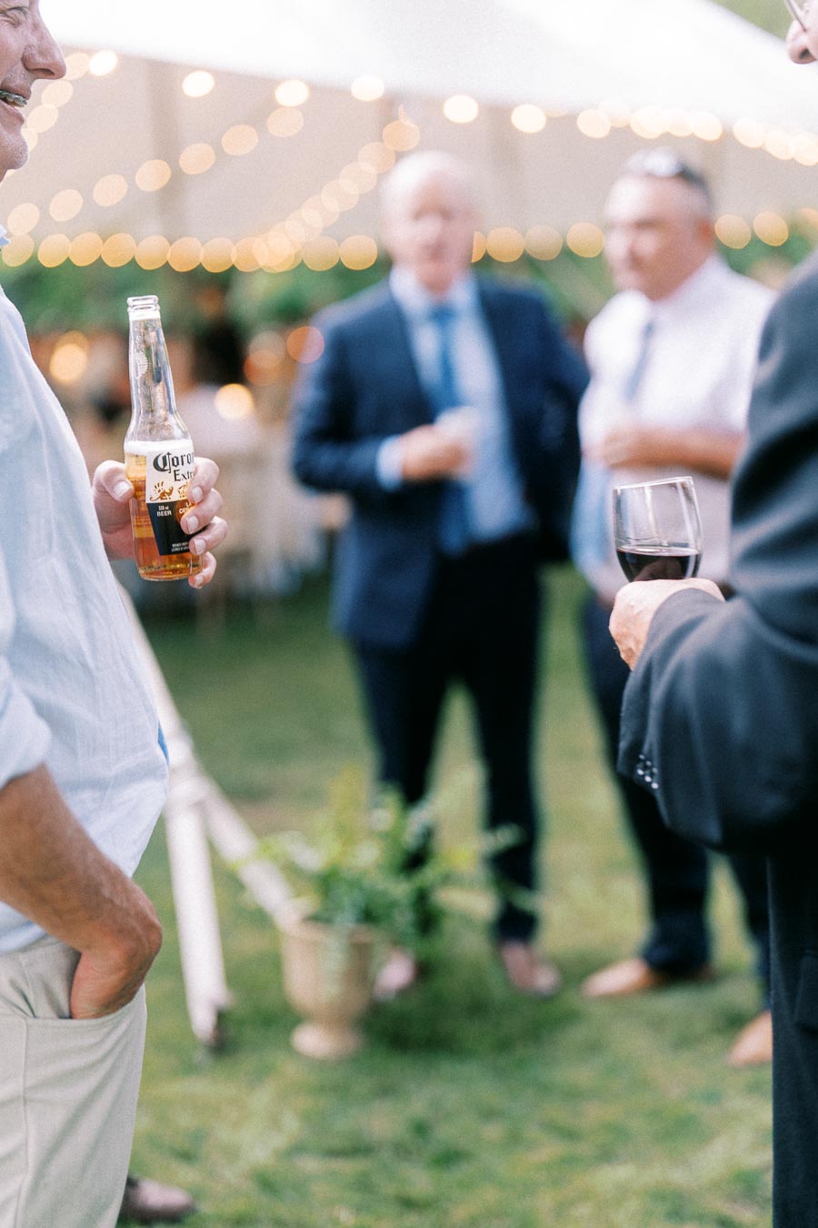 Wedding guests holding drinks under a tent with string lights at a private estate farm wedding near Chatham-Kent, Ontario, Canada.
