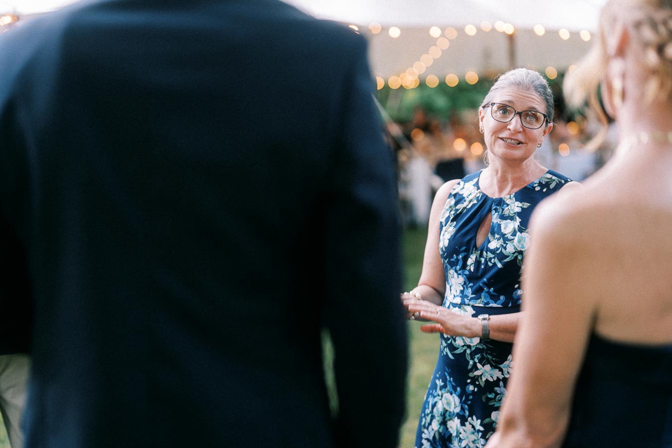 Woman in glasses talks with wedding guests during an outdoor tented farm wedding reception near Chatham-Kent, Ontario, Canada.
