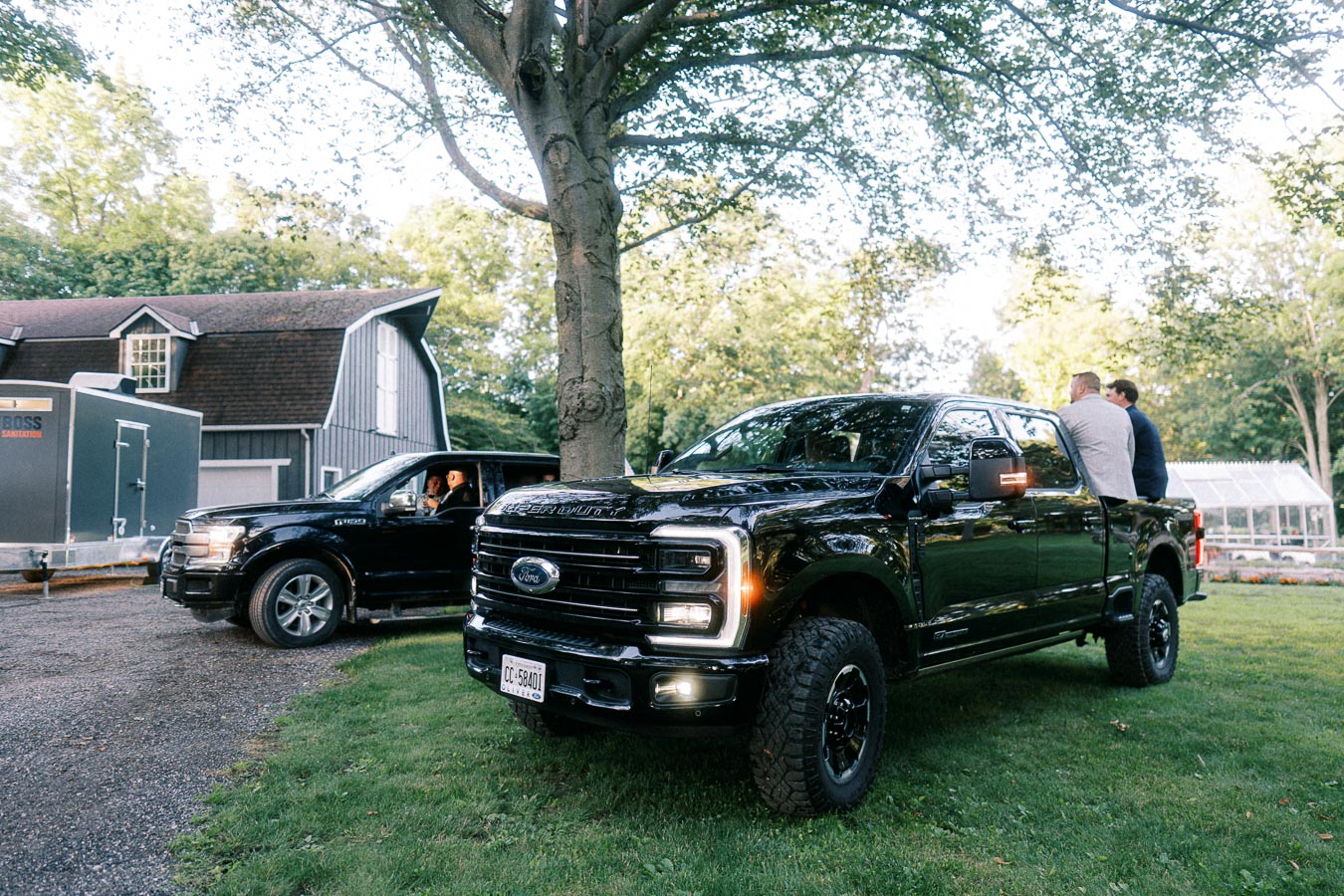 Black Ford pickup trucks parked on grass beside a barn and greenhouse at a private estate farm near Chatham-Kent, Ontario, Canada.