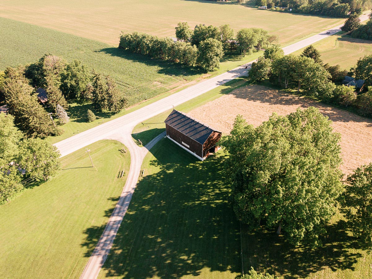 Aerial view of a rural private estate near Chatham-Kent, Ontario, with a barn, fields, road, lawns, and mature trees in summer sunlight.