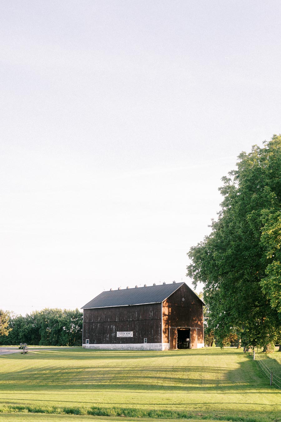 Wooden barn on a green private estate lawn near Chatham-Kent, Ontario, with trees and warm evening light for an outdoor farm wedding setting.