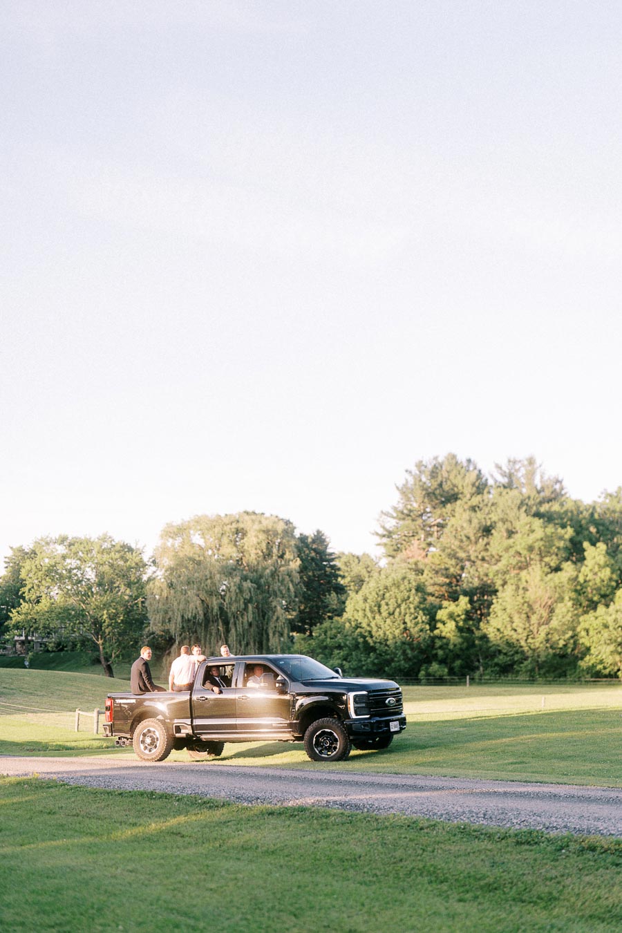 Black Ford pickup truck carrying wedding guests along a gravel driveway on a green private estate near Chatham-Kent, Ontario.