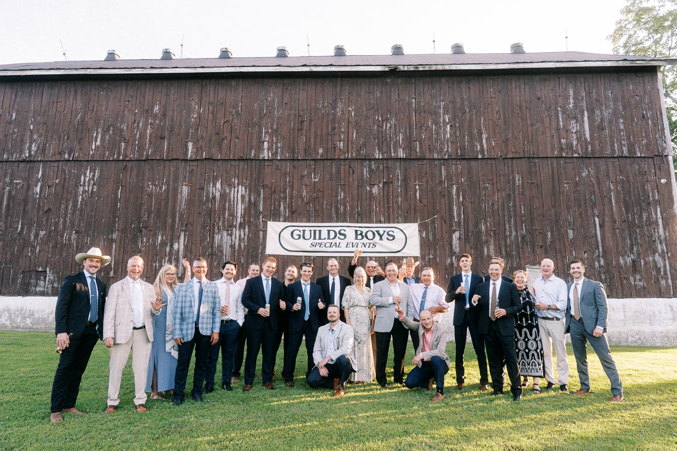 Wedding guests pose on a lawn in front of a rustic wooden barn at a private farm estate near Chatham-Kent, Ontario, Canada.