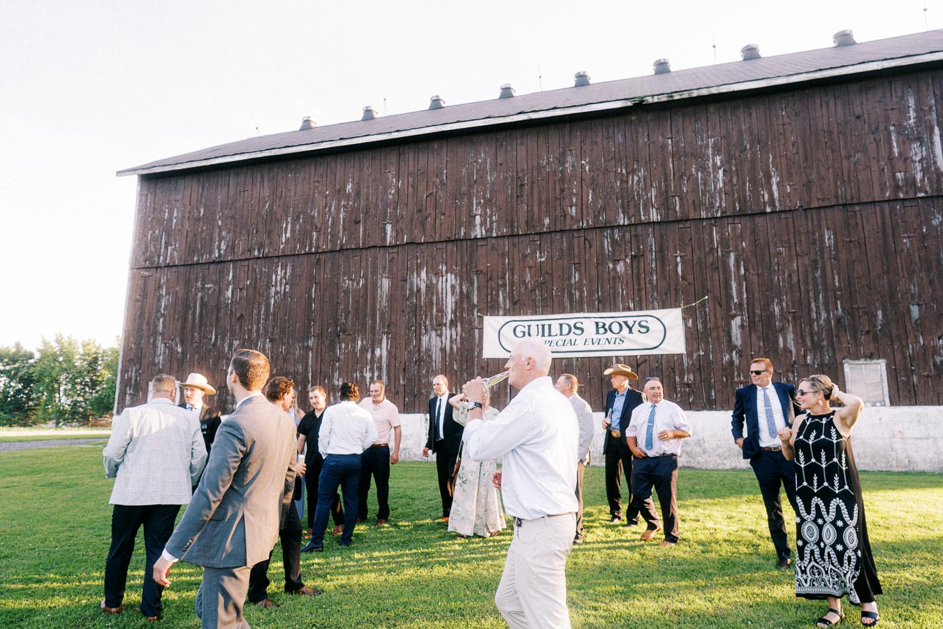 Wedding guests gather on a lawn beside a rustic wooden barn at a private farm estate near Chatham-Kent, Ontario, Canada.
