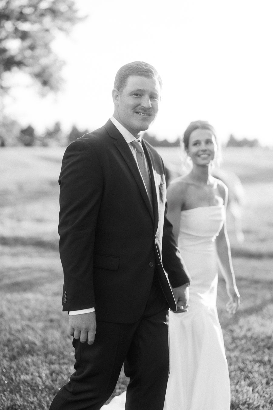 Black and white outdoor wedding portrait of bride and groom holding hands on a farm field near Chatham-Kent, Ontario, Canada.