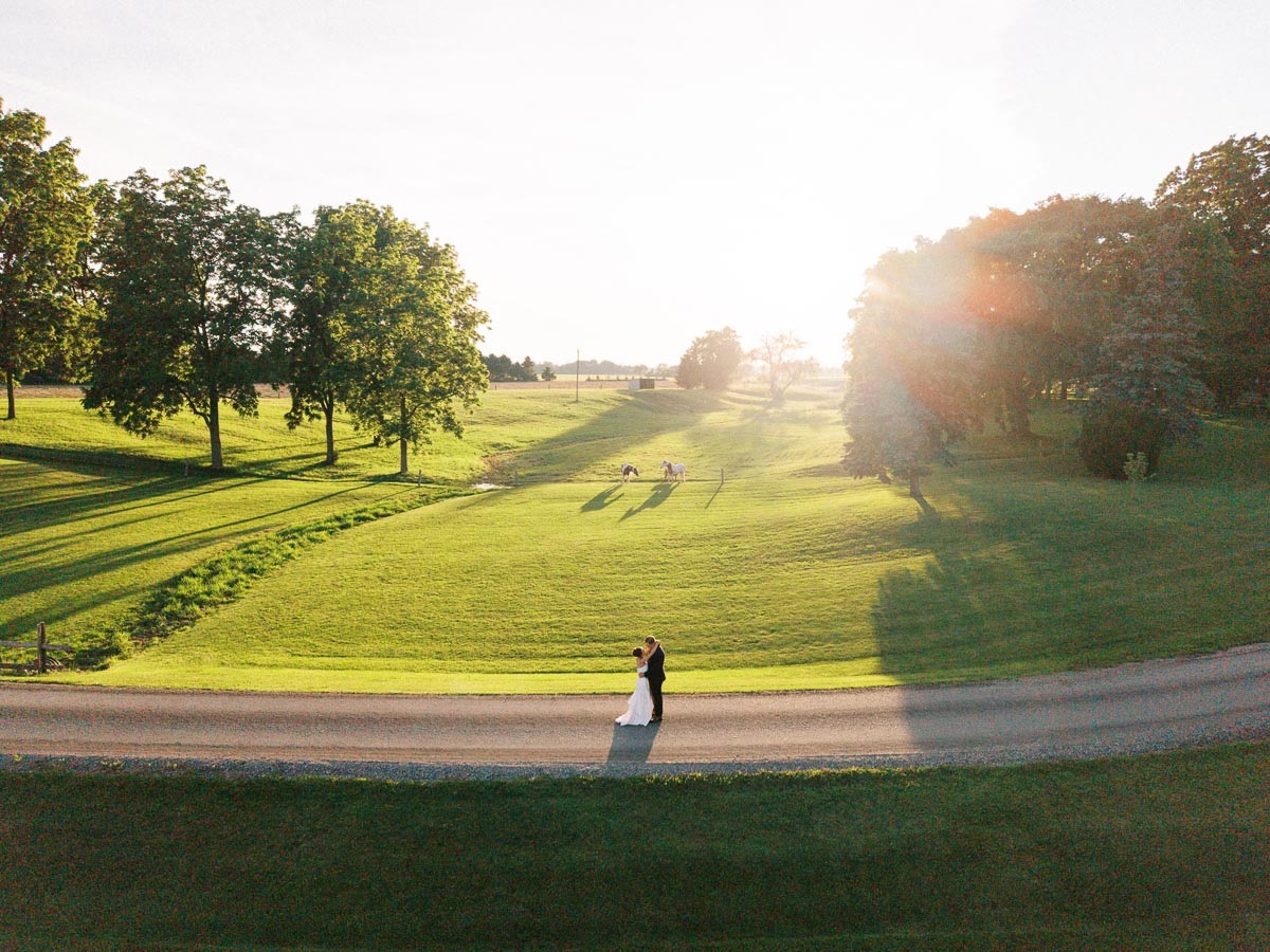 Bride and groom embracing on a gravel road at sunset on a private farm estate near Chatham-Kent, Ontario, Canada.