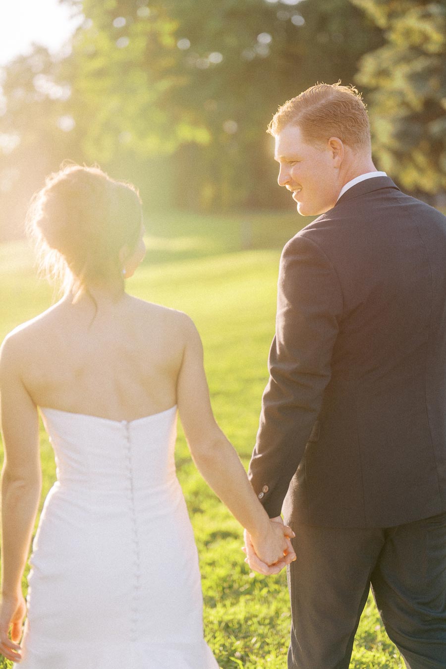 Bride and groom holding hands while walking outdoors in warm sunset light on a private estate near Chatham-Kent, Ontario, Canada.