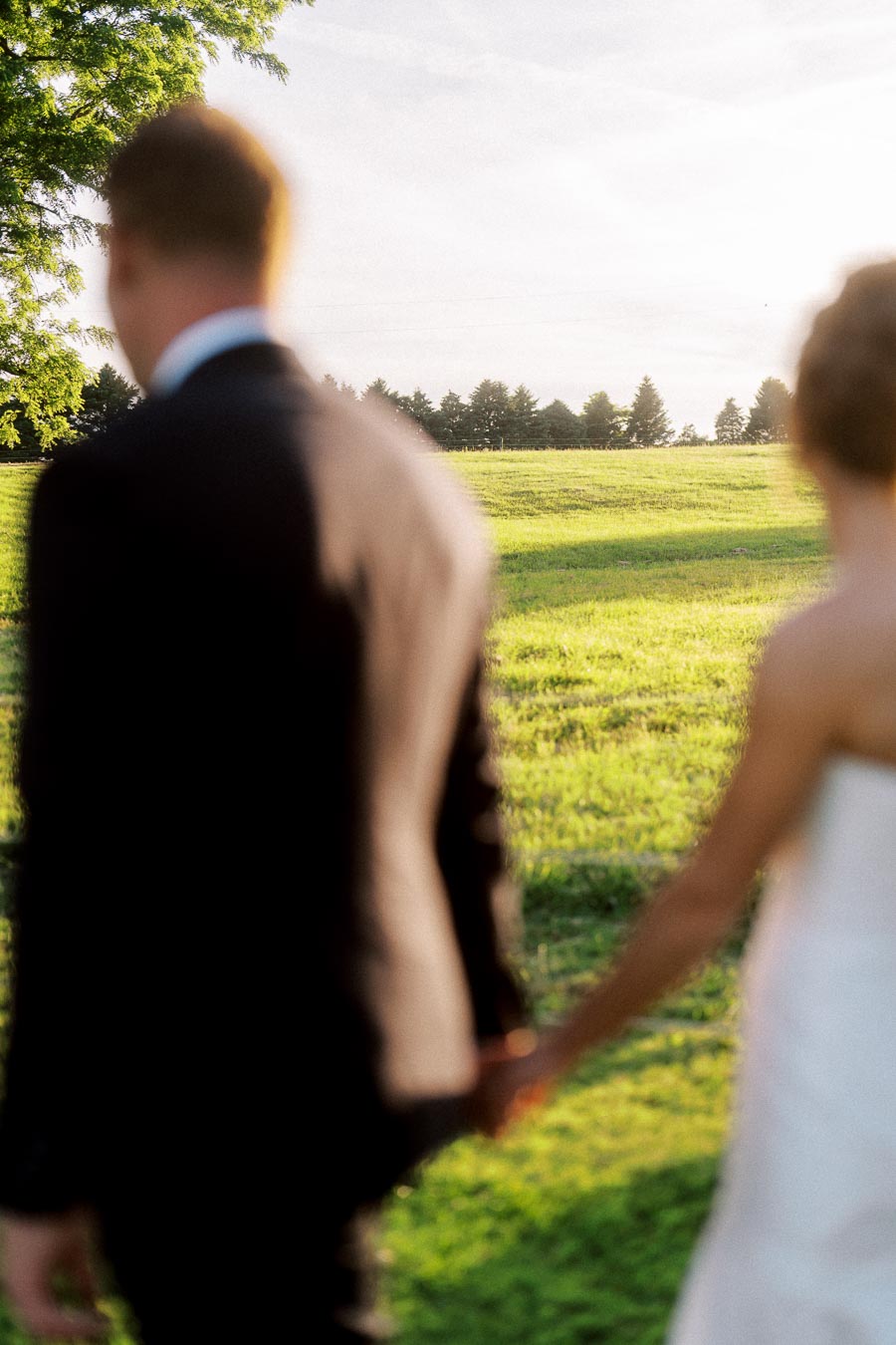 Blurred bride and groom holding hands in a sunlit farm field near Chatham-Kent, Ontario, Canada during an outdoor private estate wedding.