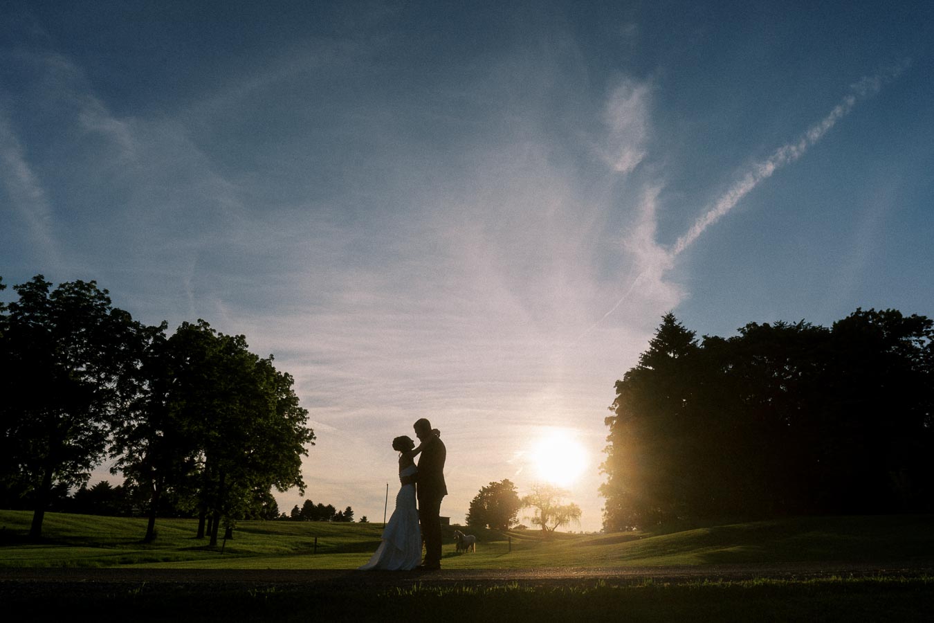 Silhouetted bride and groom standing together at sunset on a private farm estate near Chatham-Kent, Ontario, Canada.