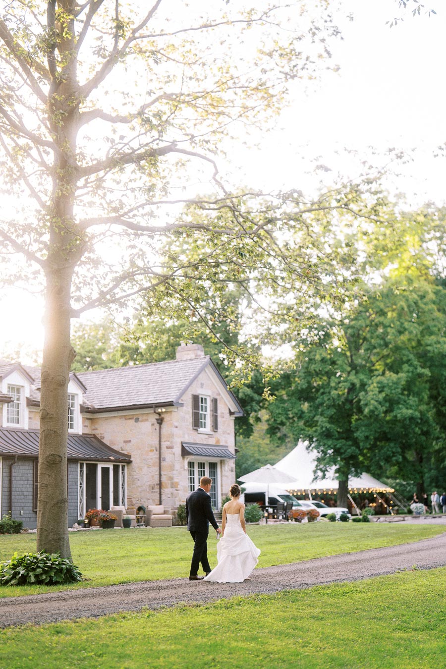 Bride and groom walking on a gravel driveway beside a private estate farmhouse with a white wedding tent in Chatham-Kent, Ontario.