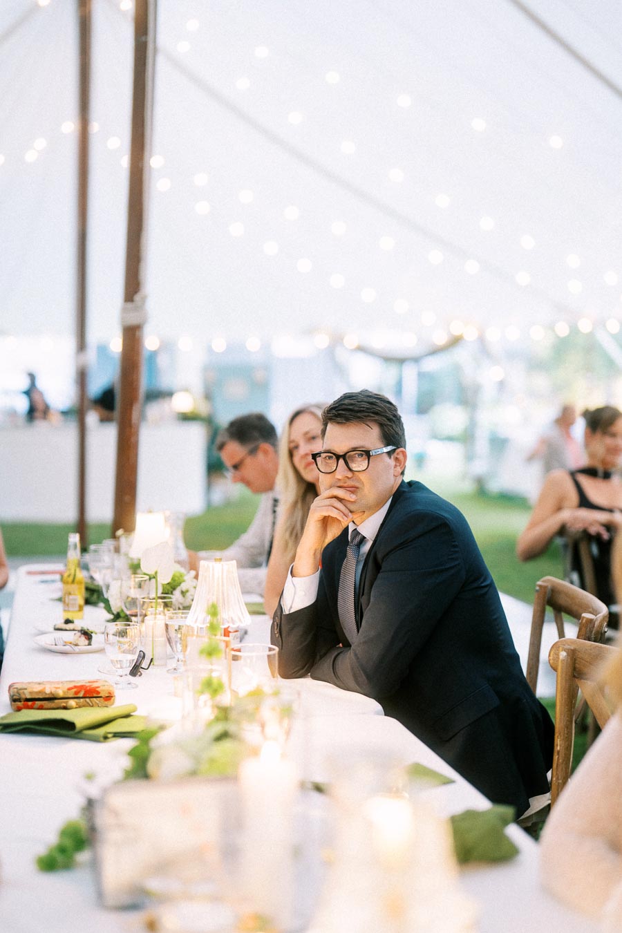 Wedding guests seated at a long dinner table inside a white reception tent with glowing string lights near Chatham-Kent, Ontario.