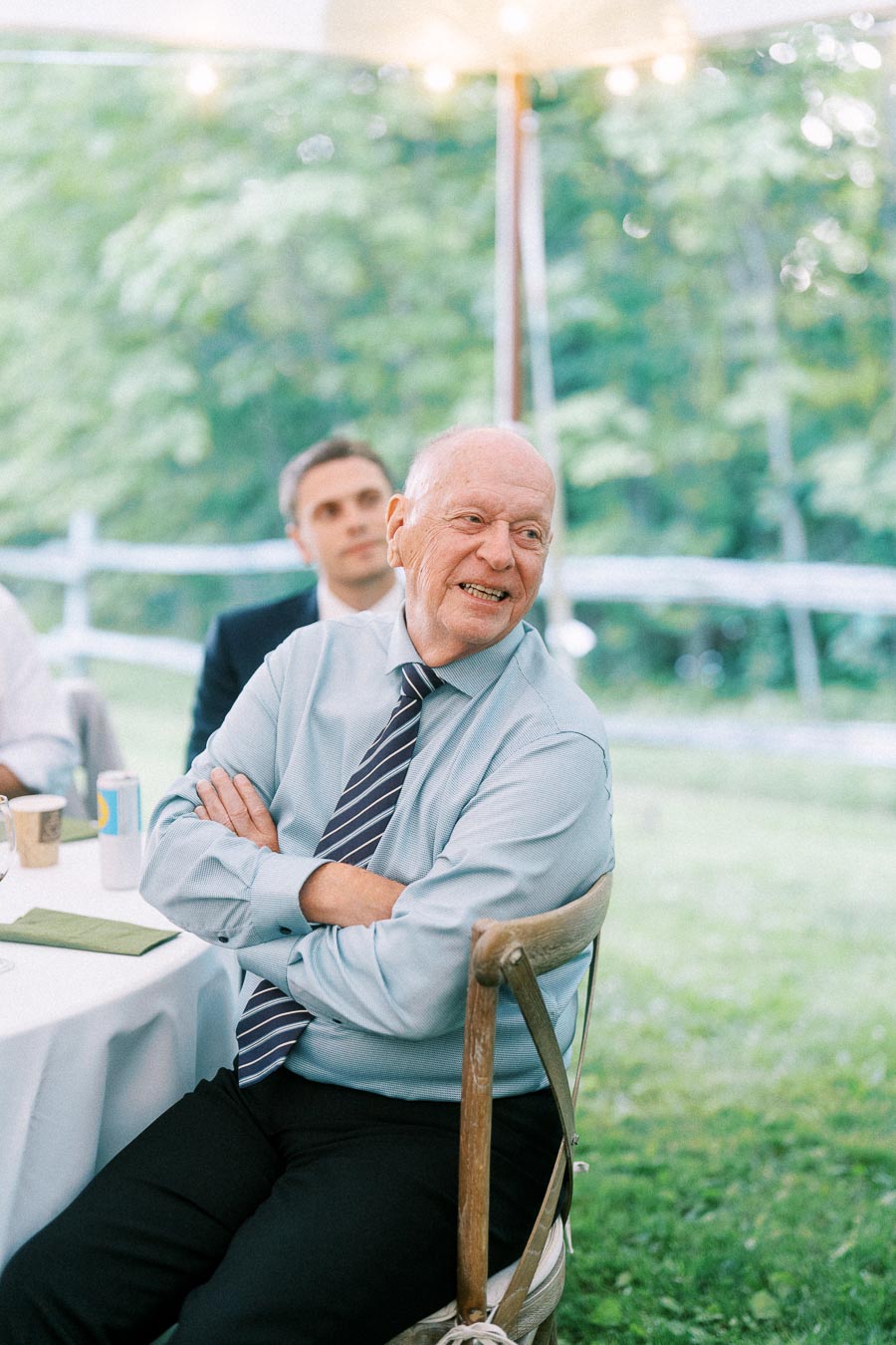 Older male wedding guest smiling at a tented outdoor reception on a private estate near Chatham-Kent, Ontario, Canada.