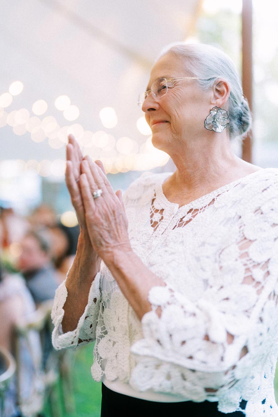 Elderly woman in a white lace blouse clapping during a tented wedding reception near Chatham-Kent, Ontario, Canada.