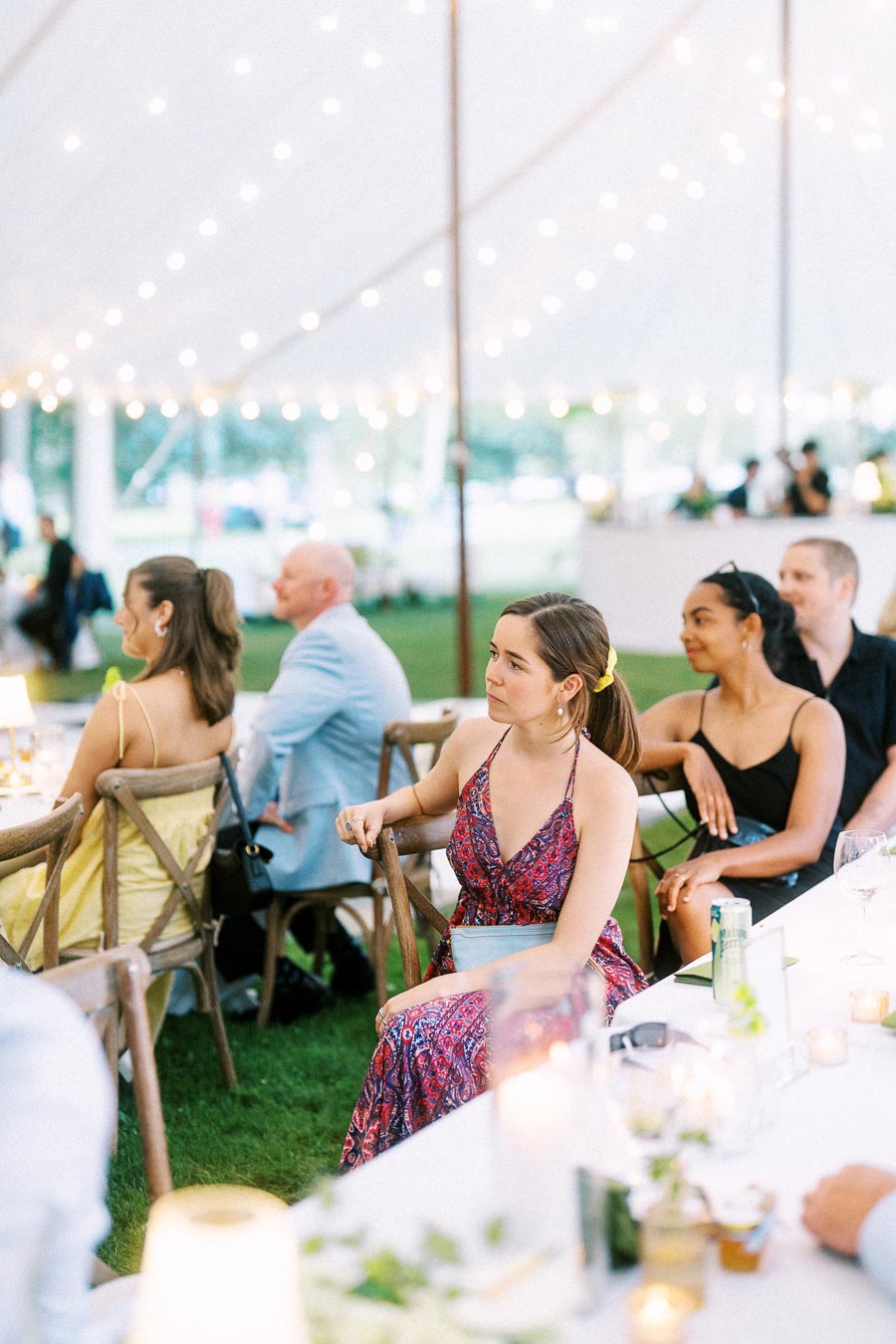 Wedding guests seated at round dinner tables under a white reception tent with string lights on a private farm estate near Chatham-Kent, Ontario, Canada.