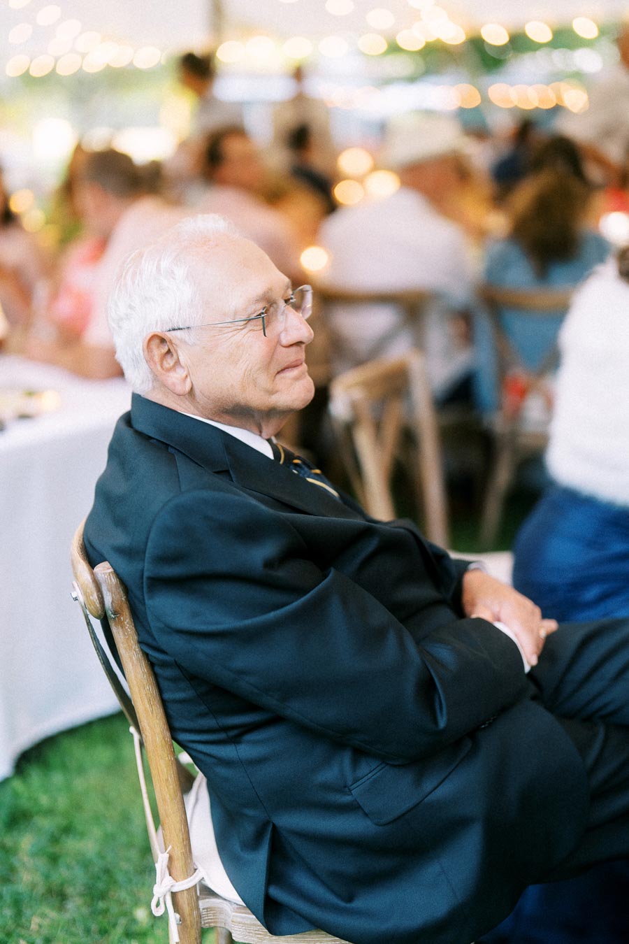 Elderly man in a dark suit seated under a wedding tent during an outdoor farm reception near Chatham-Kent, Ontario.