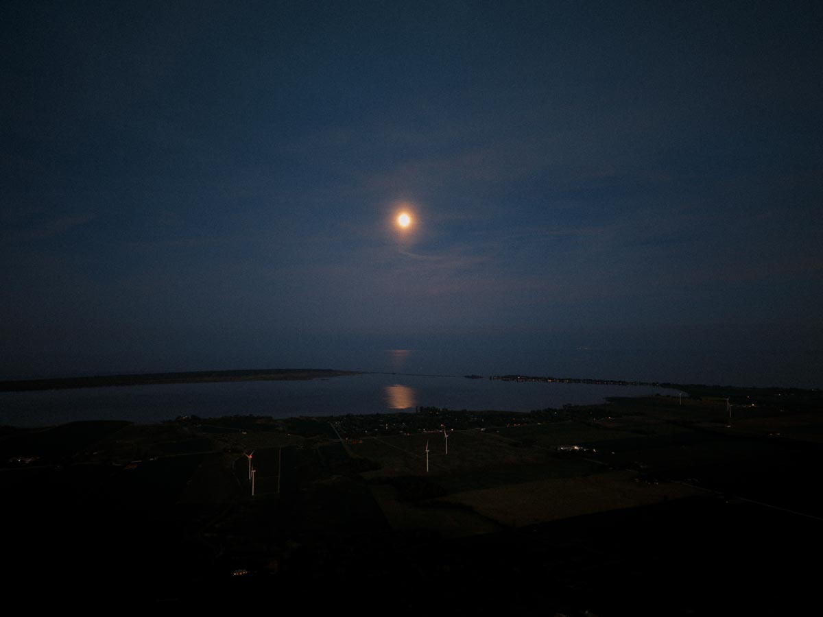 Moonlit aerial landscape near Chatham-Kent, Ontario, with water, farmland, and wind turbines under a dark evening sky.