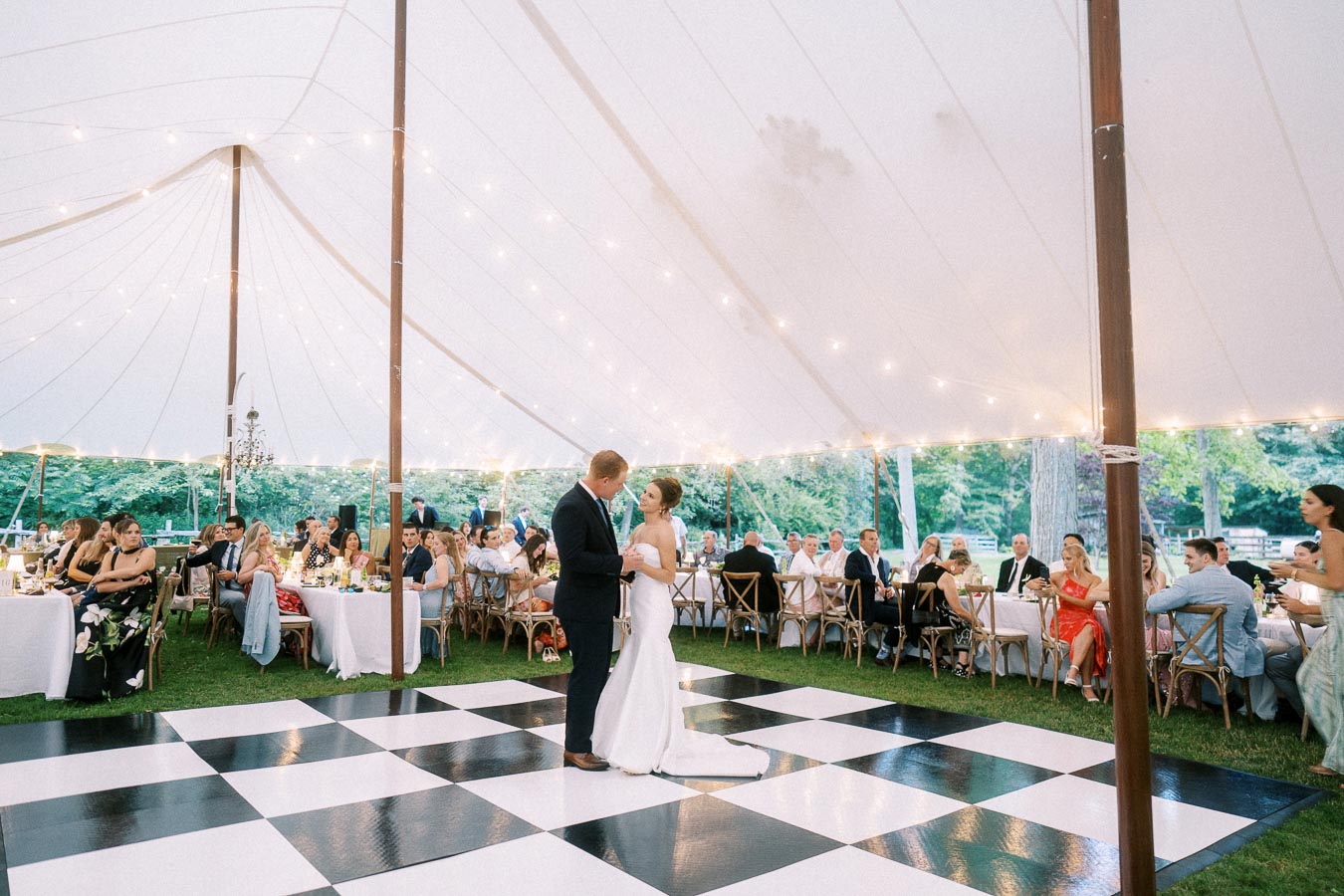 Bride and groom dancing on a black and white checkered floor under a white wedding tent with guests at farm estate reception in Chatham-Kent, Ontario.