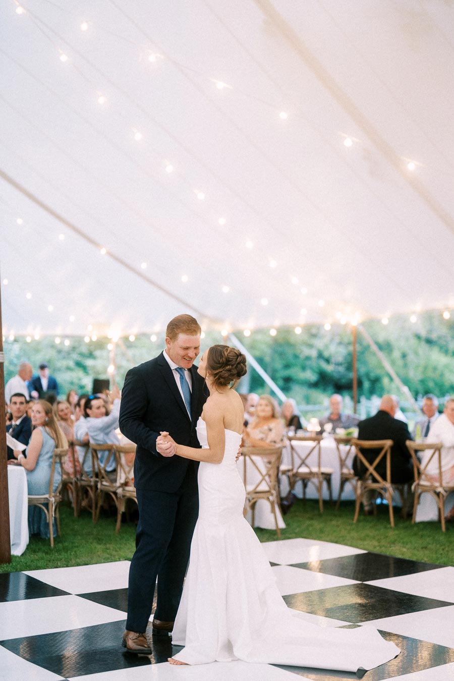 Bride and groom dancing on a black and white checkered floor under a tent with string lights during an outdoor wedding reception in Chatham-Kent, Ontario.