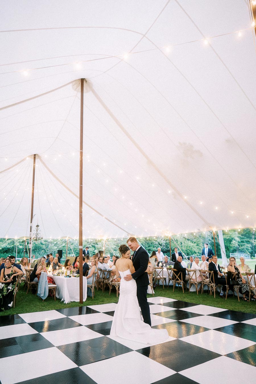 Bride and groom share a first dance on a black and white checkered floor under a glowing wedding tent near Chatham-Kent, Ontario.