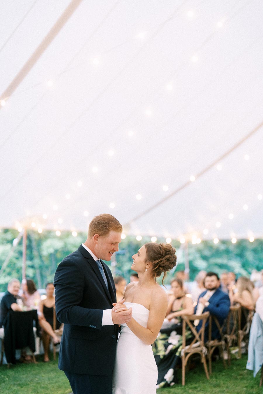 Bride and groom dancing together under a white wedding tent with string lights and seated guests at a farm reception near Chatham-Kent, Ontario.