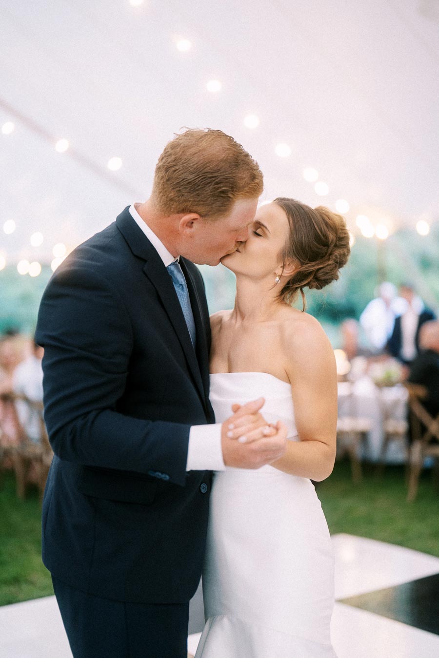 Bride and groom kissing during a first dance under a white reception tent with string lights near Chatham-Kent, Ontario, Canada.