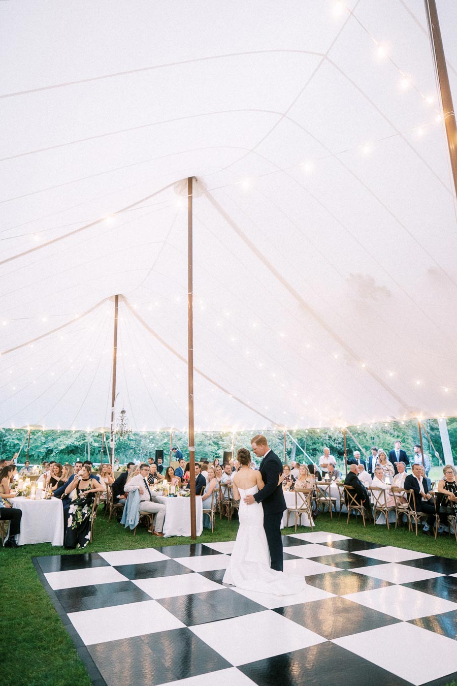 Bride and groom first dance under a white wedding tent on a checkered dance floor during a farm estate reception near Chatham-Kent, Ontario.