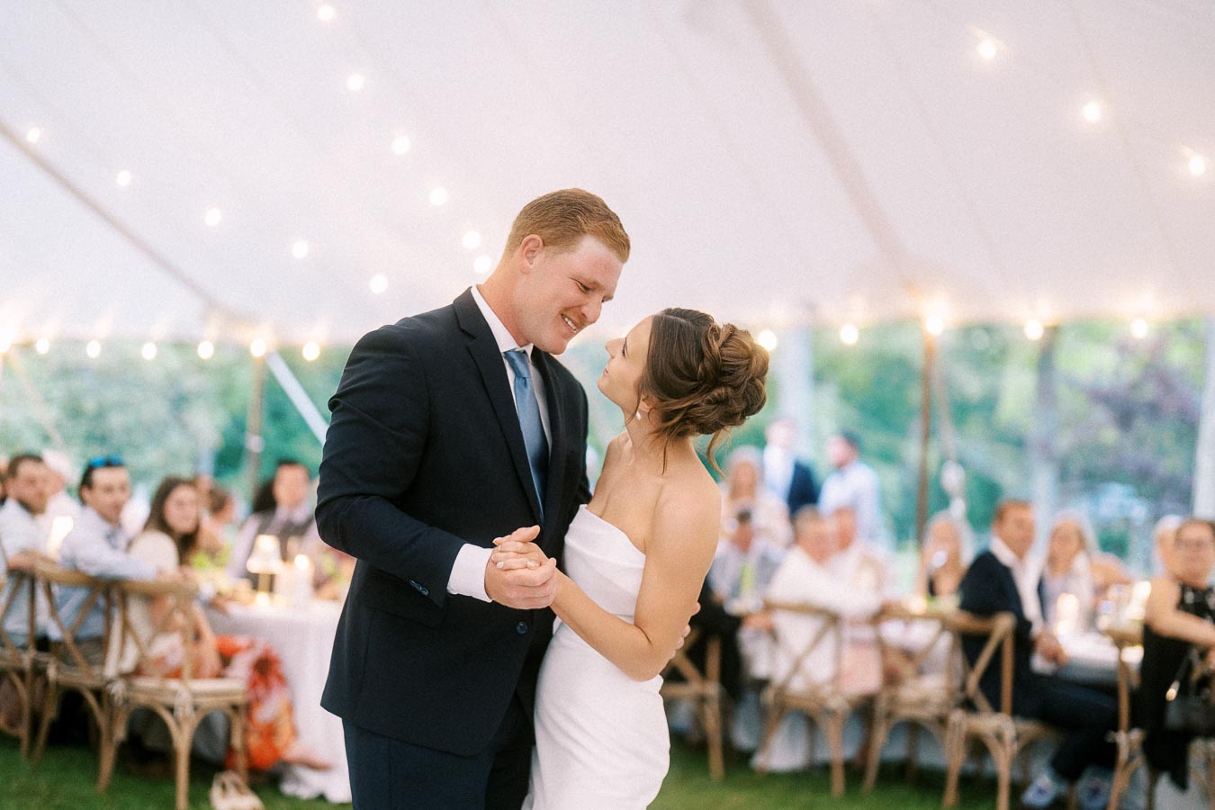 Bride and groom sharing a first dance under a white wedding tent with string lights and seated guests at a private estate farm wedding near Chatham-Kent, Ontario.