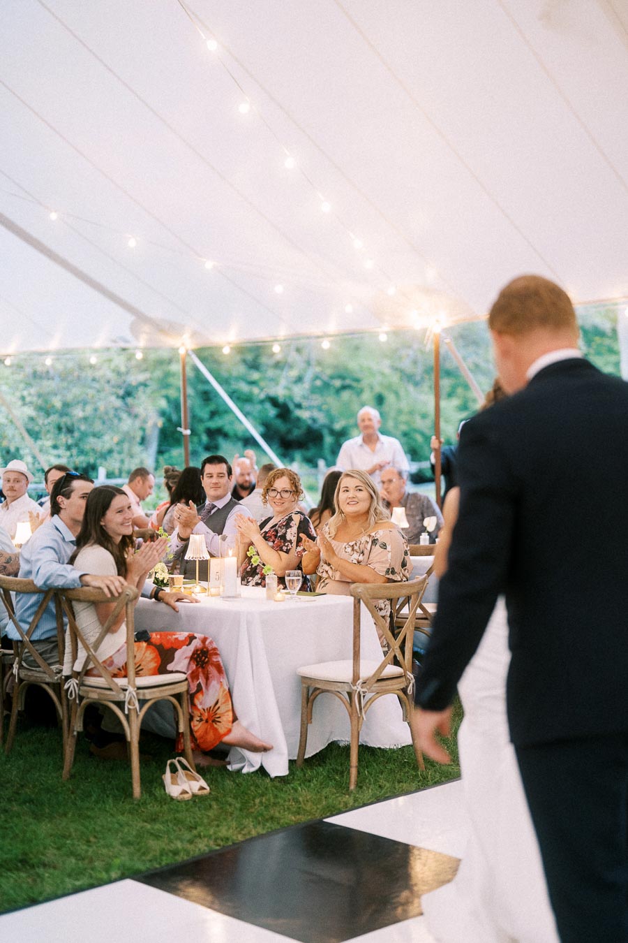 Wedding guests applaud during a tented outdoor reception on a private estate near Chatham-Kent, Ontario, with the couple entering beside a dance floor.