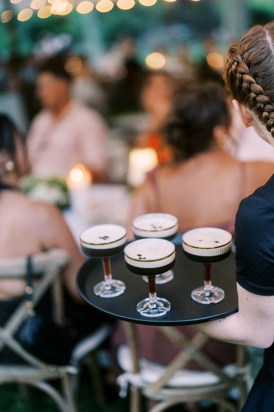 Server carrying four espresso martinis on a tray during an outdoor tented wedding dinner near Chatham-Kent, Ontario.
