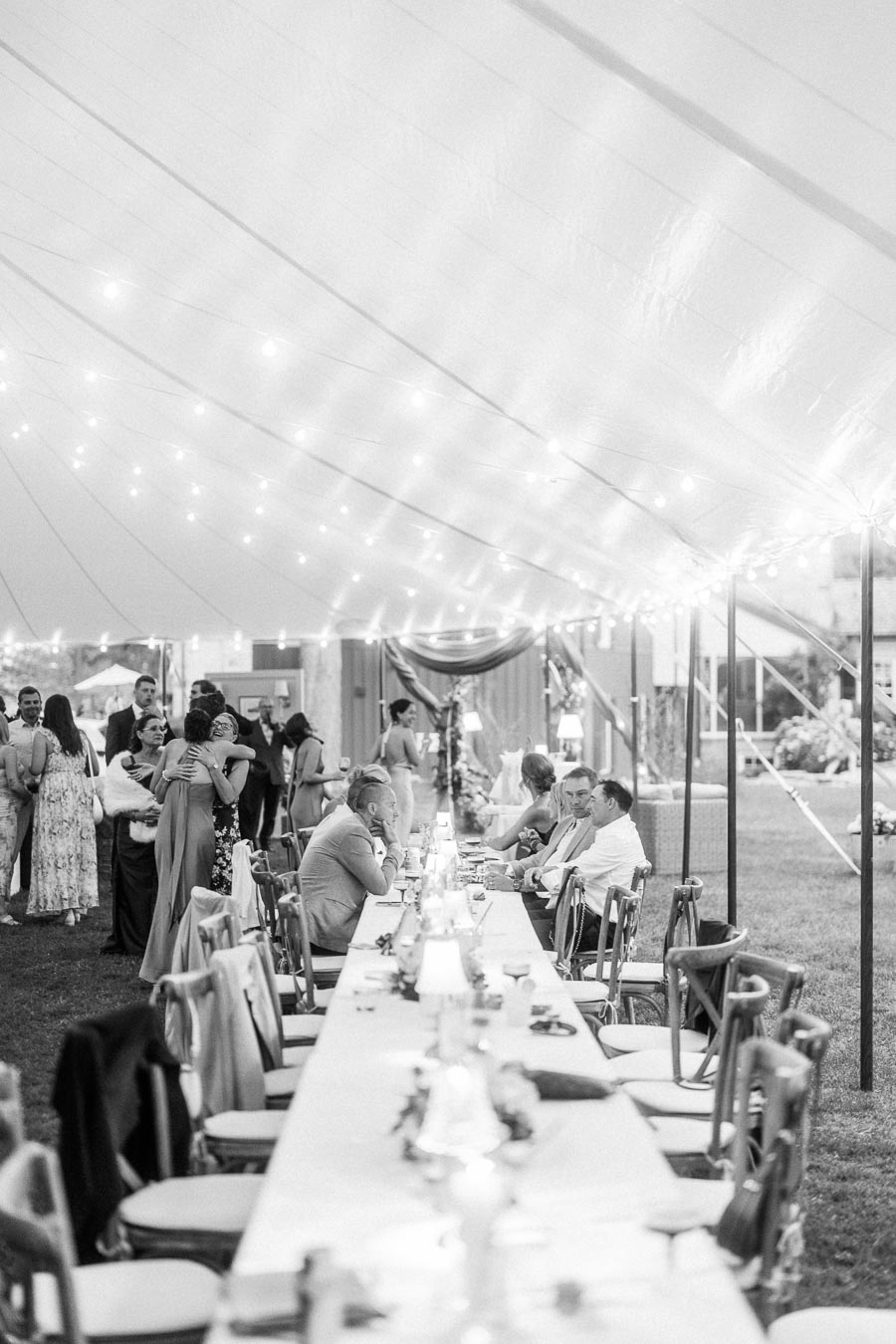 Black and white photo of wedding guests dining and socializing under a lit reception tent on a private farm estate near Chatham-Kent, Ontario.